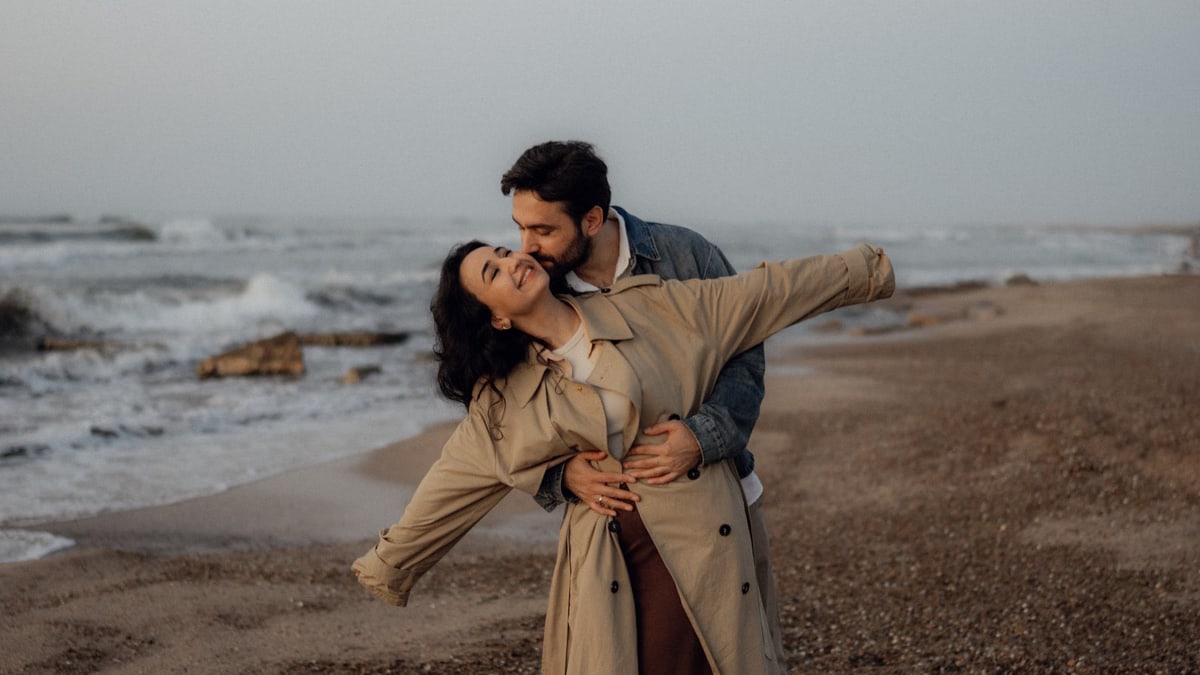 A loving couple shares a tender embrace on a serene beach, capturing a moment of happiness.